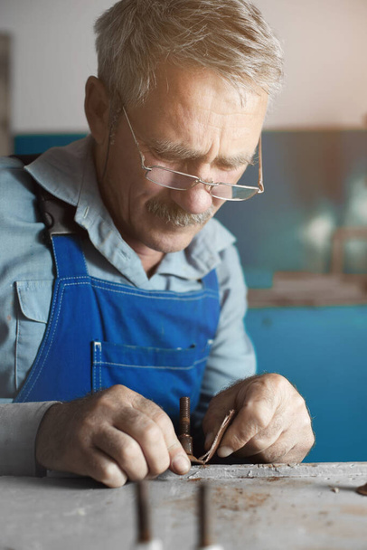 Ein älterer Herr mit Brille bei der Arbeit. Ein weißer alter Mann kaukasischen Aussehens sitzt an einem Tisch und arbeitet mit seinen Händen - Foto, Bild
