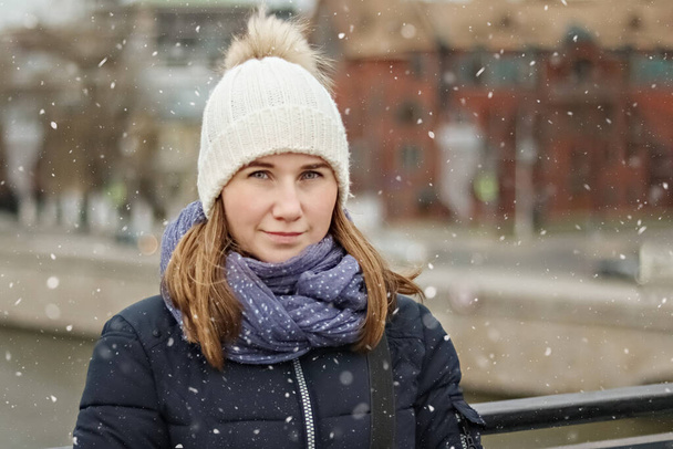 Portré egy fiatal, gyönyörű, boldog mosolygós lányról a város hátterében. Téli divat, karácsonyi ünnepek koncepció - Fotó, kép
