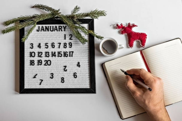 Masaüstünde yeni yıl, takvim ve Noel ağacı süslemeleri için not alan kalem ve not defteri olan bir erkek. - Fotoğraf, Görsel