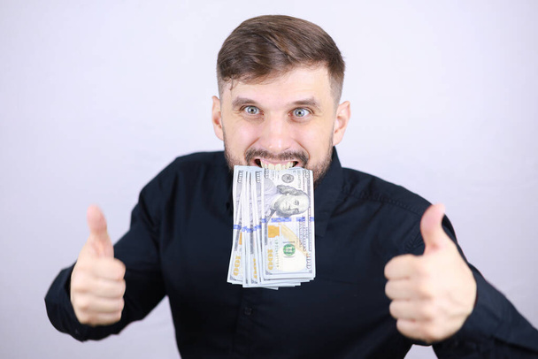 Ein männlicher Geschäftsmann hält Geld in den Zähnen und drückt den Daumen nach oben - Foto, Bild