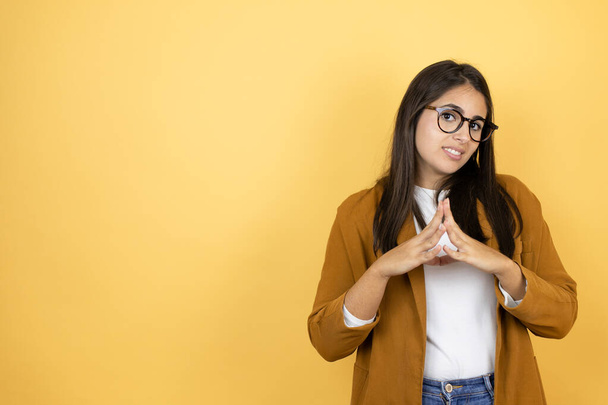 Young beautiful woman wearing a blazer over isolated yellow background with Hands together and fingers crossed smiling relaxed and cheerful. Success and optimistic - Photo, Image