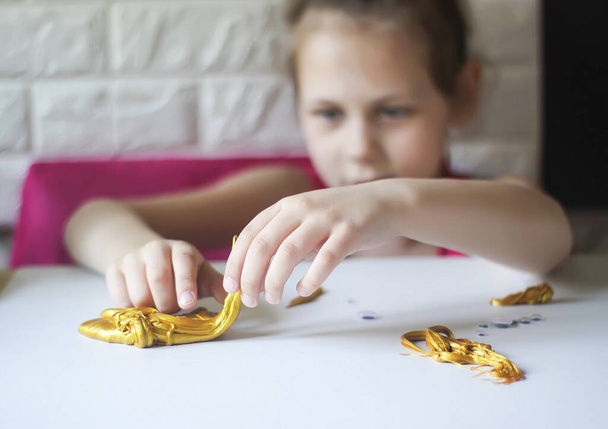 Маленька дівчинка грає з золотим слизом. Сенсорна активність для дитини
. - Фото, зображення