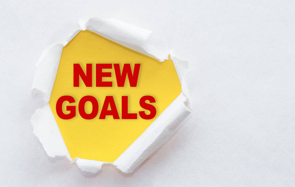 Top view of white torn paper and the text "NEW GOALS" on a yellow background. Business motivation, inspiration concept. New Year goals and resolutions setting. - Foto, afbeelding