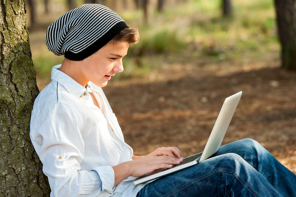 Adolescente menino socializando no laptop ao ar livre
. - Foto, Imagem