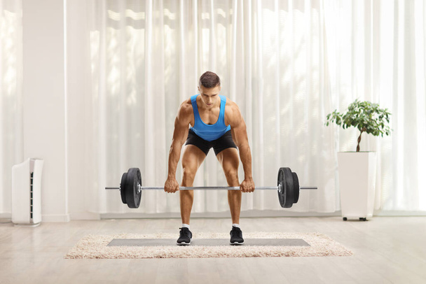 Strong young man lifting heavy weights and looking at camera at home - Photo, Image