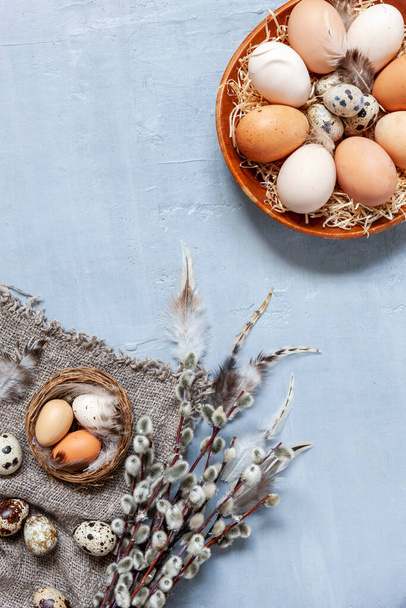 Chicken  and  Quail eggs on a plate with willow on a light gray background. Pattern with straw and feathers. - Fotografie, Obrázek
