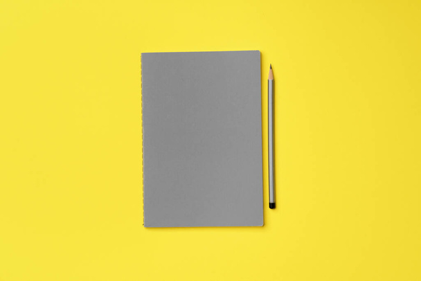 Bloc de notas gris con lápiz sobre fondo amarillo - Foto, Imagen