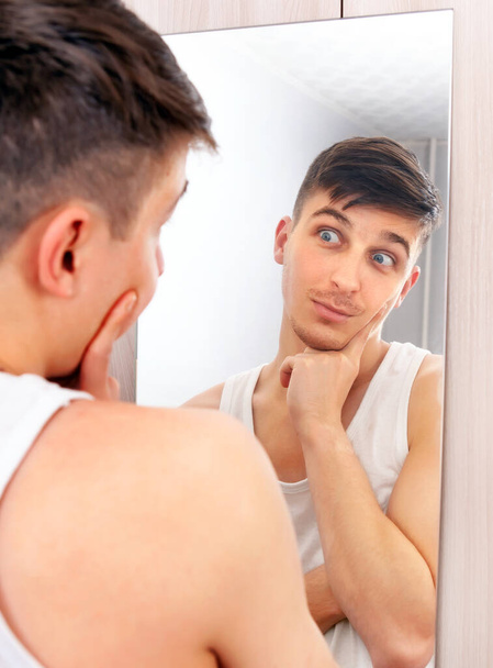 Surprised Young Man looking to Reflection in the Mirror in the Room - 写真・画像