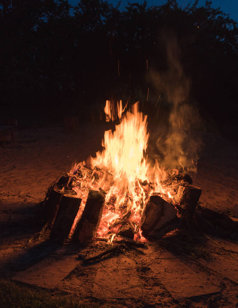 κοντινή φωτιά, μεγάλα φλεγόμενα κομμάτια ξύλου και φλόγες κόκκινης φωτιάς στο θερινό ηλιοστάσιο - Φωτογραφία, εικόνα