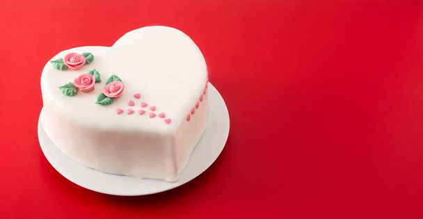 Herzkuchen zum Valentinstag, Muttertag oder Geburtstag, dekoriert mit Rosen und rosa Zuckerherzen auf rotem Hintergrund - Foto, Bild