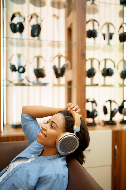 Šťastná žena poslouchá hudbu v obchodě se sluchátky. Žena osoba v audio shopu, vitrína se sluchátky na pozadí, kupující v multimediálním salonu - Fotografie, Obrázek