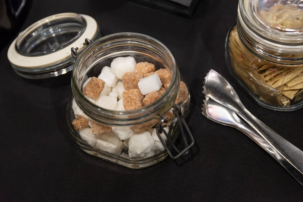 Ciotola di vetro con zucchero bianco e marrone grumo e pinze sul tavolo per tè e caffè, colazione in hotel. - Foto, immagini