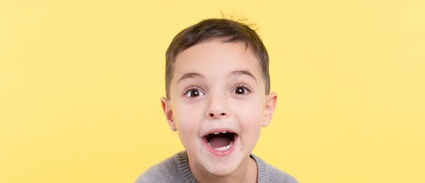 Retrato emocional de un niño sobre un fondo amarillo. El rostro entusiasta está cerca. Contacto visual. Visión, idea brillante, concepto publicitario. Luz del estudio. Combinación de moda de gris y amarillo en 2021 - Foto, imagen