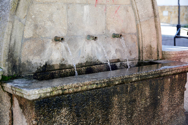 Kamenná fontána se třemi vodovodními trubkami. Přírodní voda tekoucí z kamenné fontány. Přírodní voda. - Fotografie, Obrázek