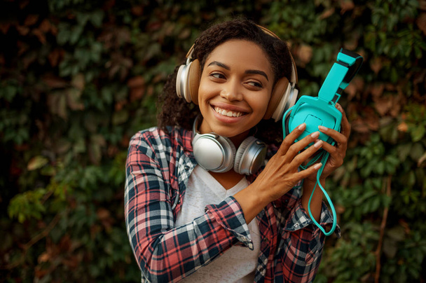 Zeneszerető a fejhallgatóban, zenét hallgat a nyári parkban. Női audiofil séta szabadban, lány fülhallgató, zöld bokrok a háttérben - Fotó, kép