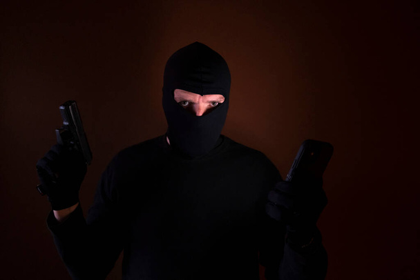 Egy kaukázusi betörő sorozata betört egy házba fegyverrel és okostelefonnal a kezében.. - Fotó, kép
