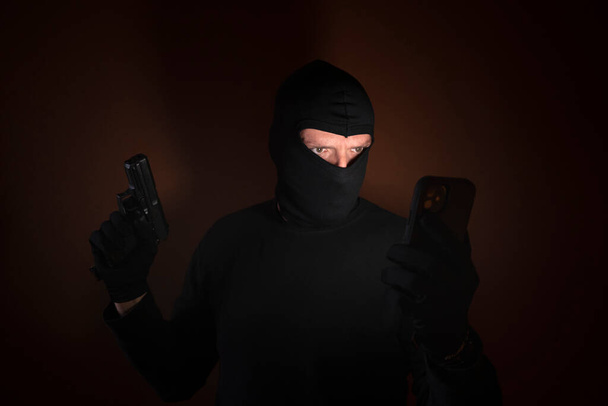 Reeks van een blanke inbreker die inbreekt in een huis met pistool en smartphone in de hand. - Foto, afbeelding