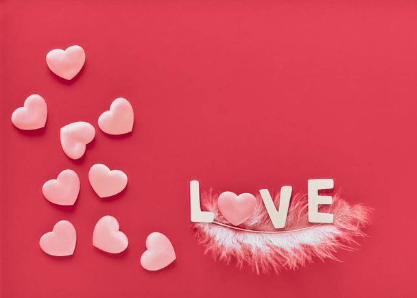 У день святого Валентина рожеве тло з рожевими серцями і словом "Любов", прикрашене білими дерев'яними буквами на білій пір'ї. День матері, 8 березня. - Фото, зображення