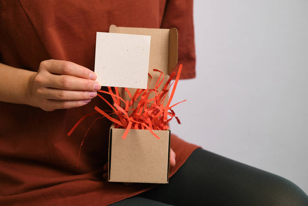 Woman has a surprise box with a postcard in her hands. Beautiful celebration packaging. Time to open holiday presents. Paper gift box. Invitation and congratulations. Blank space in postcard - Fotografie, Obrázek