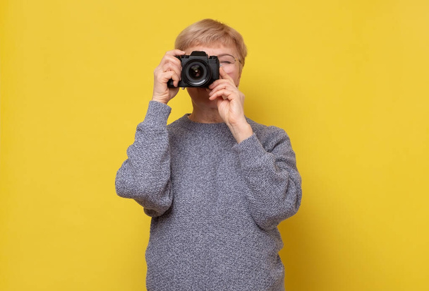 Sarı arka planda fotoğraf makinesi olan olgun bir kadın fotoğrafçı.. - Fotoğraf, Görsel