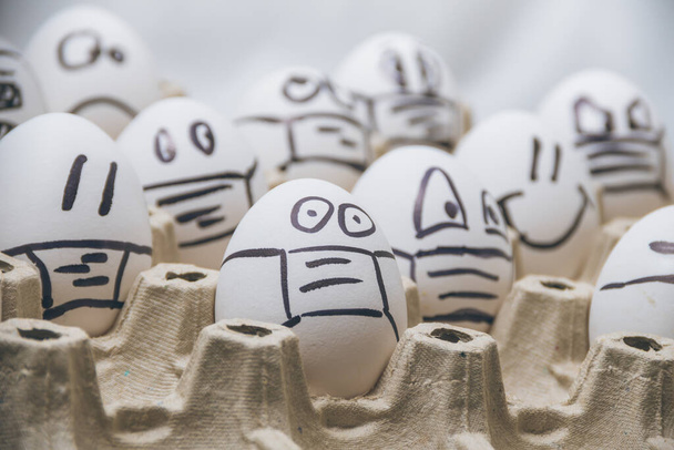 concept of canceling easter because of oronavirus qarantine. close up of chicken easter eggs with doodle scared faces wearing medical masks with white background. - 写真・画像