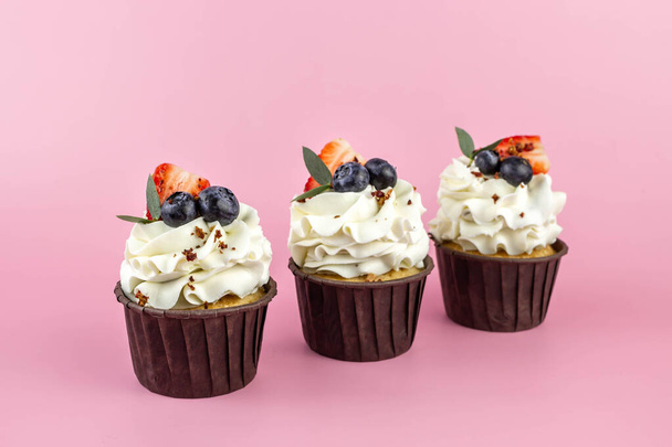 Deliciosos cupcakes con crema y bayas frescas aisladas sobre fondo rosa. Copiar espacio. - Foto, imagen