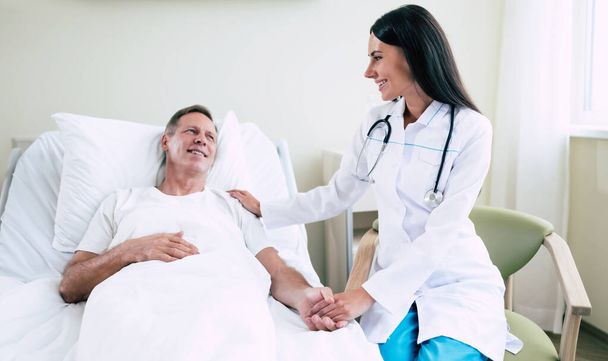 Médico mulher confiante feliz com um estetoscópio está falando com o paciente homem na enfermaria do hospital - Foto, Imagem