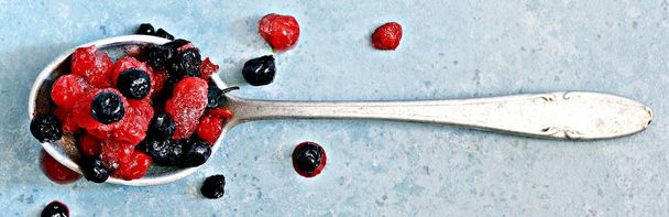 Zamrożone (rozmrożone) wiśnie, jagody, czerwone porzeczki w łyżce na niebieskim tle. Zdrowe owoce, domowe preparaty do przygotowywania koktajli, kompot, napój owocowy, przeciery owocowe. - Zdjęcie, obraz