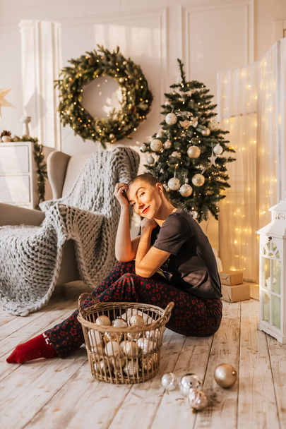 Όμορφη χαρούμενη ευτυχισμένη νεαρή κοπέλα στο πάτωμα με πιτζάμες με χριστουγεννιάτικα παιχνίδια κοντά στο δέντρο του νέου έτους στο σπίτι - Φωτογραφία, εικόνα