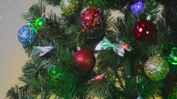 Na světle a žlutém pozadí zelený vánoční stromek zdobený hračkami a girlandami - Záběry, video