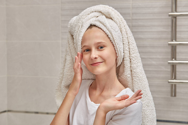 Smiling girl in the bathroom doing morning treatments in a towel on her head. - Foto, Imagen