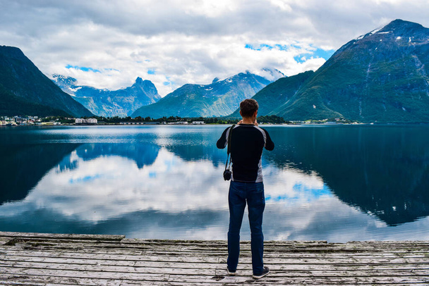 Mann Wanderer fotografiert schöne Landschaft von Bergen spiegelt sich in Romsdal Fjord (Romsdalsfjord) bei bewölktem Wetter. More og Romsdal county. Blick von der Stadt Andalsnes. Sommerreiseabenteuer nach Norwegen - Foto, Bild