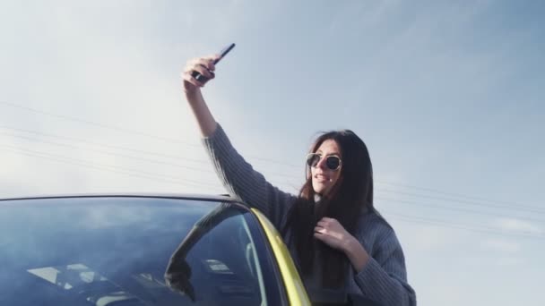 Young woman with sunglasses leaned out of the car window and records self video selfie stories - Footage, Video