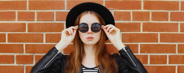 Portrait of stylish young woman model wearing a black rock style over a brick wall background - Фото, зображення