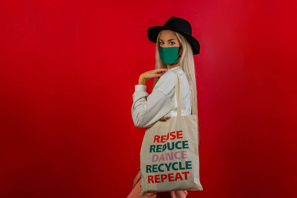 Fashionable girl shopping with recycled bag and green mask for prevention from coronavirus Covid19 pandemic. Red background. Concept recycle - Photo, Image