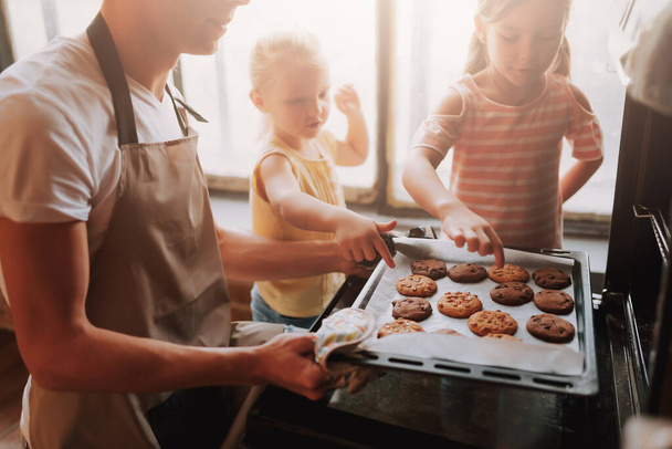 Oříznutý obrázek mladého otce se dvěma roztomilými dcerami vařícími v kuchyni. Rodina dělá sušenky společně doma. - Fotografie, Obrázek