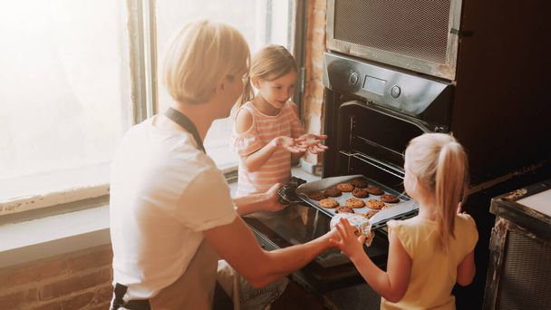 Młody ojciec z dwoma uroczymi córkami gotującymi w kuchni. Rodzinne ciasteczka razem w domu. - Zdjęcie, obraz