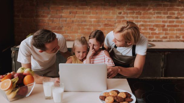 Gay couple with their adopted cute daughters reading recipe on laptop and cooking on kitchen. Lgbt family at home. - Foto, imagen