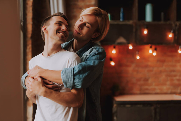 Любящая гей-пара дома. Два красивых мужчины обнимаются и целуются на кухне. Концепция ЛГБТ. - Фото, изображение