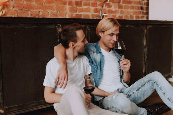 Rakastava homopari kotona. Kaksi komeaa miestä halaa, suutelee ja juo viiniä keittiössä. LGBT-käsite. - Valokuva, kuva