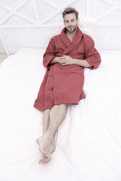 Knowing how to relax. Handsome man lying in bed to relax after bath. Sleepy guy in red bathrobe taking time to relax in morning. Its time to relax - Foto, imagen