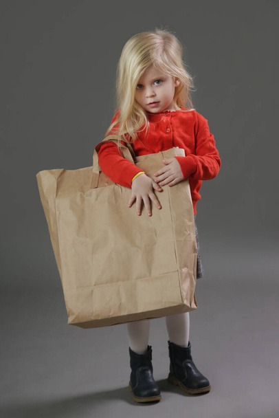 Studio portrait of adorable 3 years old girl holding big blank paper bag.  - Foto, Imagen