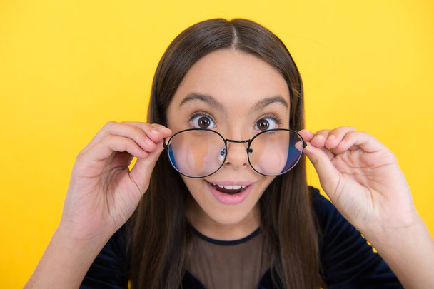 niña inteligente sorprendido con el pelo largo y gafas en el fondo amarillo, sorpresa - Foto, Imagen