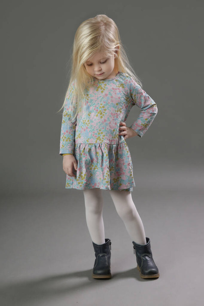 Fashion studio portrait of adorable 3 years old blonde girl in floral pattern dress on grey background. - Foto, Imagen