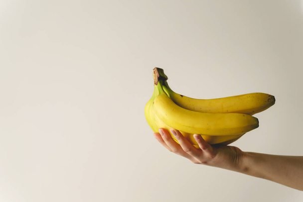 白い壁の前にバナナを持っている未知の白人女性の手の上に閉じる-健康的な有機食品新鮮な果物の概念コピースペース - 写真・画像