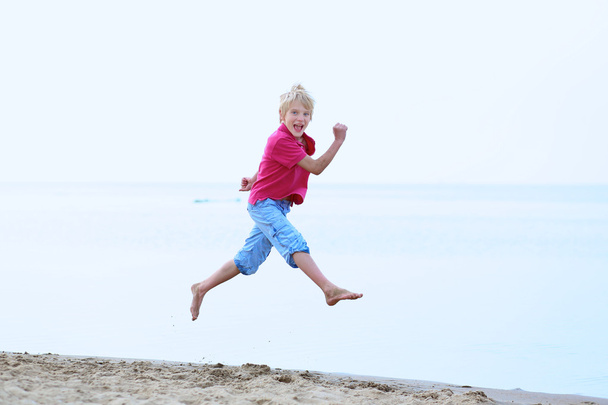 Happy active teenager boy having fun jumping on the beach - Photo, image