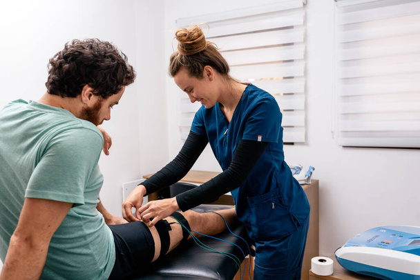 Stockfoto van een vrouwelijke werknemer die een man die in een brancard zit behandeling tegen pijn in zijn been geeft. - Foto, afbeelding