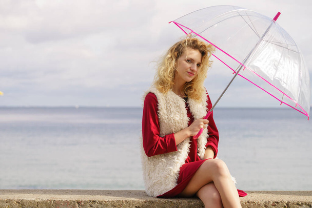 Happy elegant adult woman holding transparent umbrella against sky. Weather forecasting concept. - Photo, Image