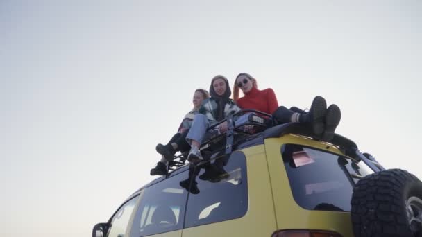 Three the best girlfriends sits on yellow car outdoors and poses on camera - Footage, Video