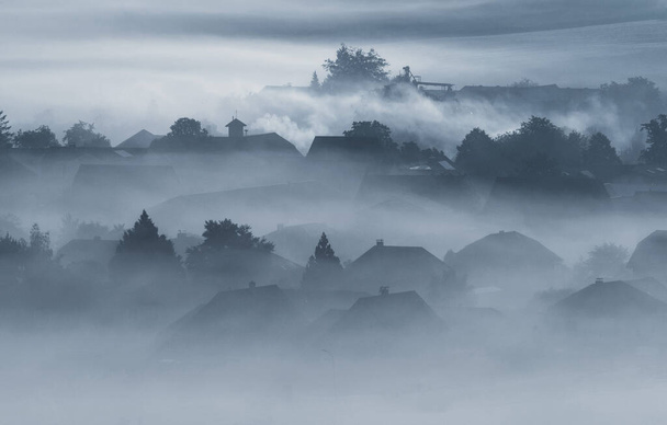 Bâtiments de villages maisons et arbres dans un brouillard dense et de faible altitude brouillard matinal maussade à Gemeinlebarn Basse-Autriche - Photo, image